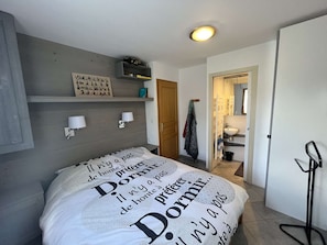 A bedroom with a bed, bedside lamps, a wall-mounted shelf, and a door leading to a bathroom. - Charming duplex apartment - 6 guests (Valloire)