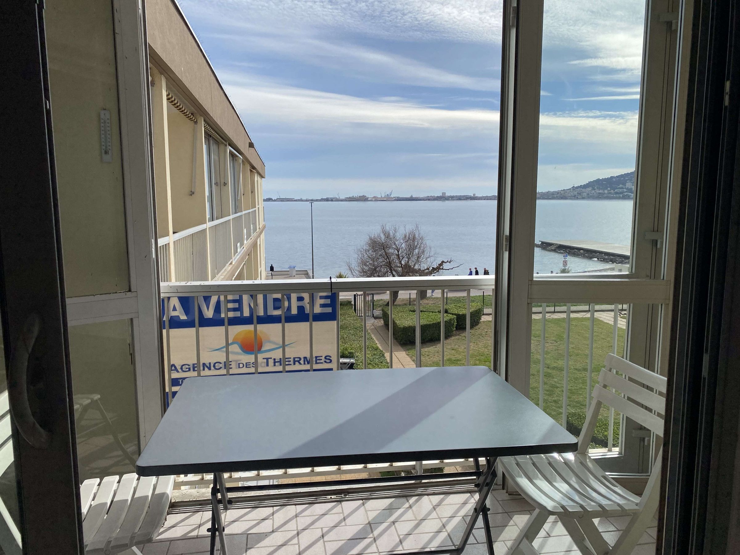 Un balcón con mesa y sillas, que da a una masa de agua con vista distante a un puente y edificios.