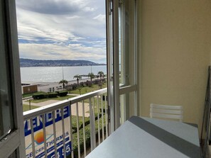 Ein Balkon mit Tisch und Stuhl, mit Blick auf einen Strand mit Palmen und einem Schild für ein Geschäft.
