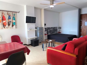 Ein Hotelzimmer mit einem Bett, einem roten Sofa, einem kleinen Tisch, einem Fernseher, einem Deckenventilator und einer Wand mit Kunstwerken.