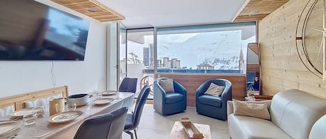 A modern living room with a dining area, a sofa, and a television mounted on the wall.