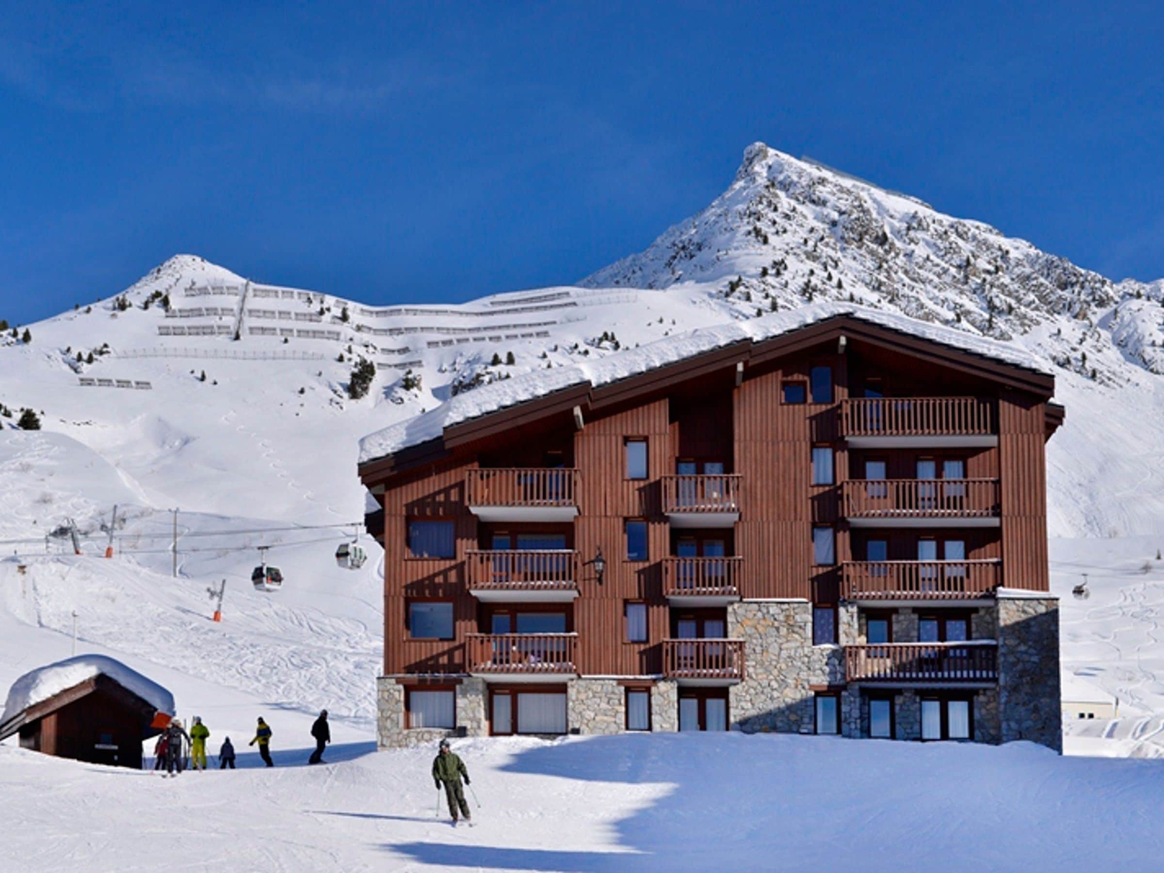 A multi-story wooden building with balconies, surrounded by snow-covered terrain and a mountain in the background.