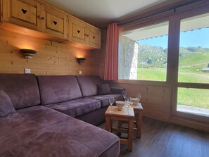 En inredning med träpanel, en soffa, ett litet bord med glas och ett fönster med utsikt över grönområden.