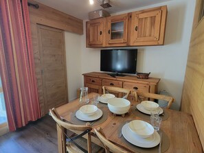 Ein Essbereich mit einem Holztisch, gedeckt für vier Personen, einem Fernseher auf einer Holzkommode und einem Fenster mit Vorhängen.