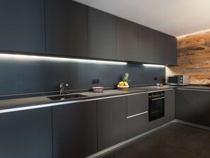 A modern kitchen with dark cabinetry, a built-in microwave, and a fruit bowl on the counter. - Modern apartment, wheelchair access - 8 guests (Courchevel 1550)
