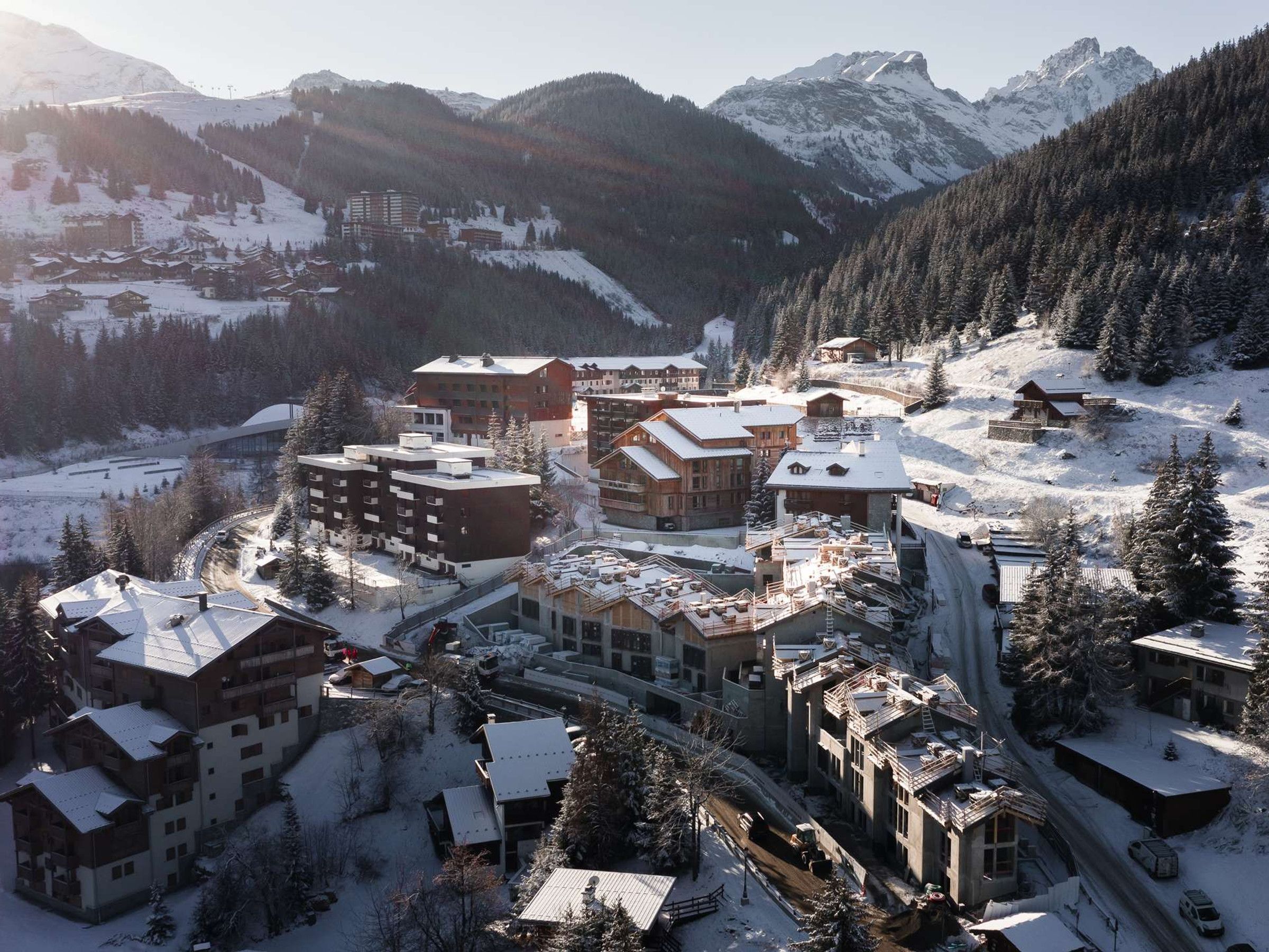 A snow-covered mountain resort with multiple buildings, including lodges and a ski lift.