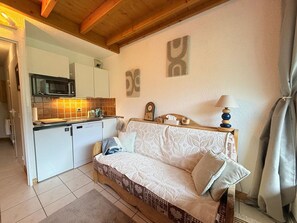 A compact living space with a kitchenette, a sofa, a bedside table with a lamp, and a clock on the wall. - Duplex at the slopes - 6 guests (Montgenèvre)
