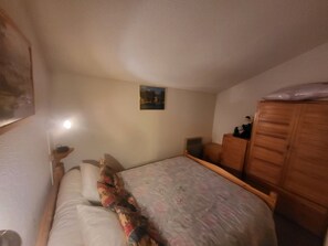 Ein Schlafzimmer mit einem Bett, einem Holzschrank, einem Nachttisch und einem an der Wand hängenden Bild.