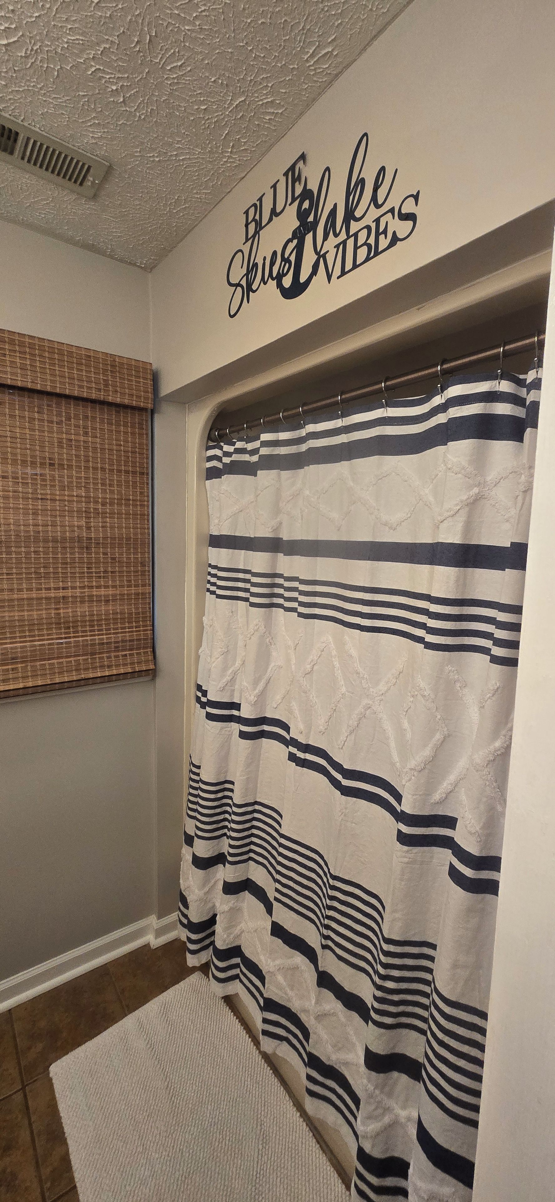 Ein Badezimmer mit gestreifter Duschvorhang, strukturierter Decke und einem Fenster mit Jalousien.