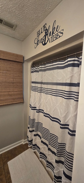 A bathroom with a striped shower curtain, a textured ceiling, and a window with blinds.