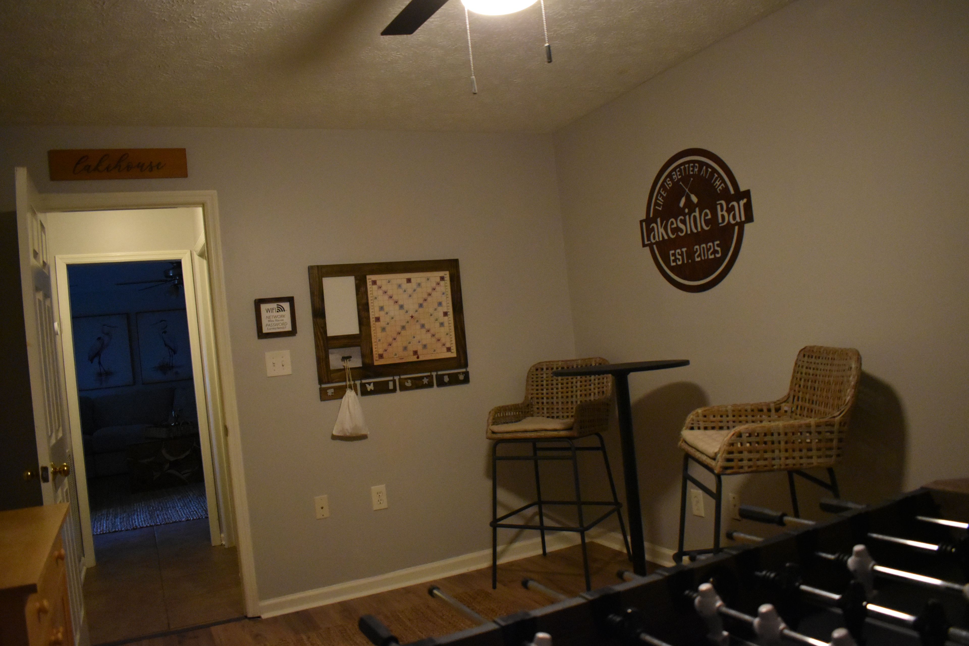Quarto com mesa de bilhar, duas cadeiras de vime, relógio de parede e placa indicando um bar.