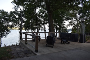 A lakeside park with a wooden deck, Adirondack chairs, and a covered grill area.