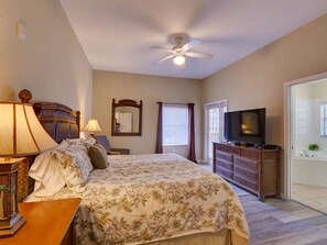 Un dormitorio con cama, televisión, ventilador de techo, cómoda y ventana con persianas.