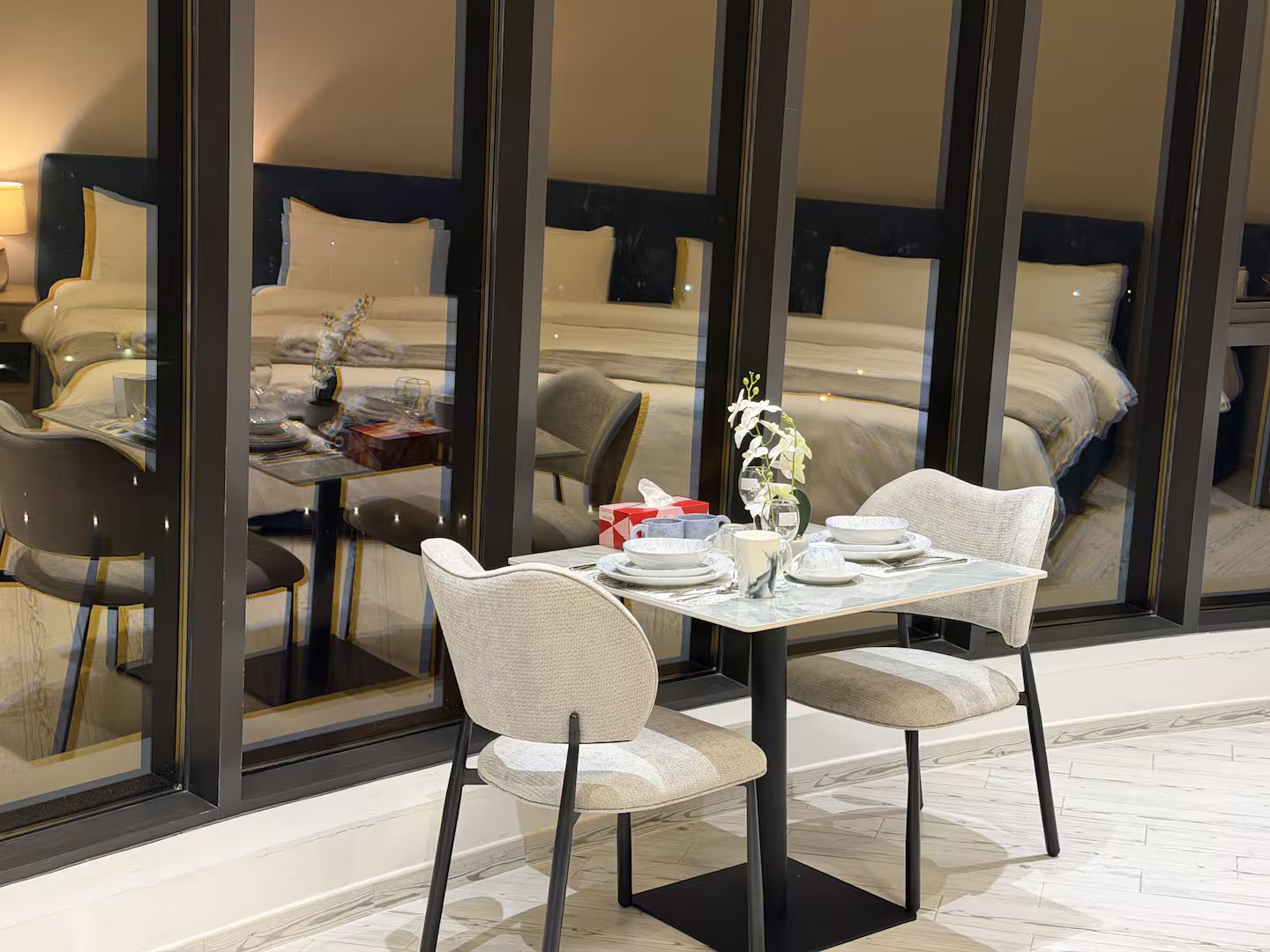 A modern hotel room with a dining area, a bed with a headboard, and a large window.