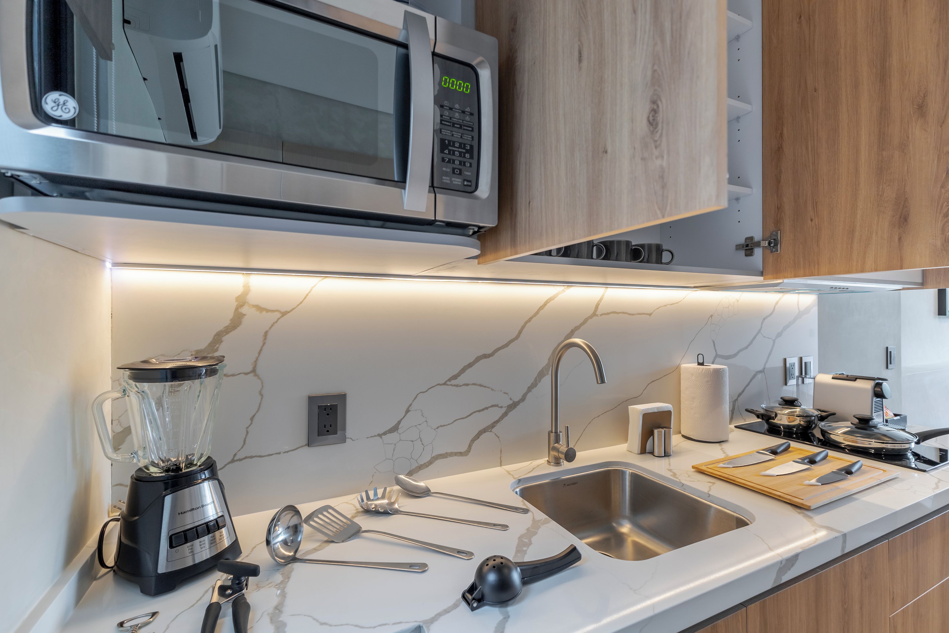 A modern kitchen with a built-in microwave, a blender, a sink, and various utensils.