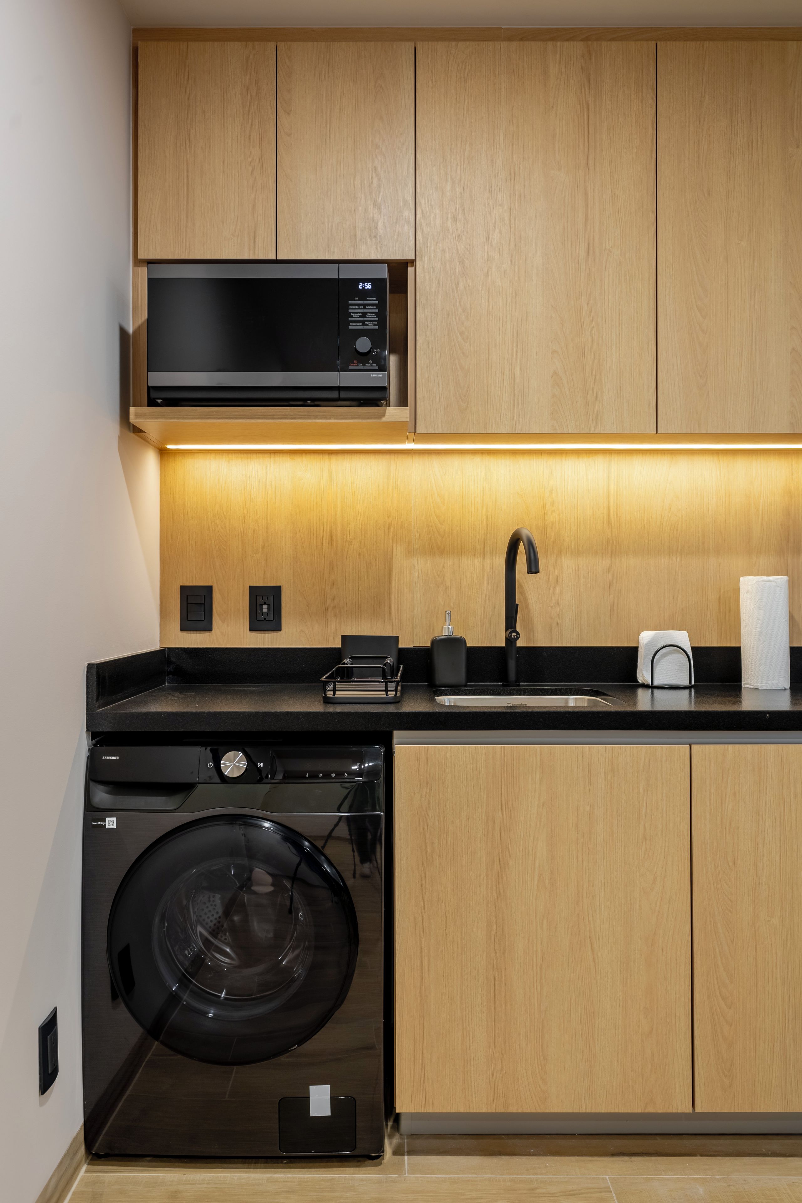 A modern kitchen with wooden cabinets, a built-in microwave, a sink with a faucet, and a front-loading washing machine.
