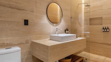A modern bathroom with a wooden vanity, a round mirror, a toilet, and a glass-enclosed shower area.