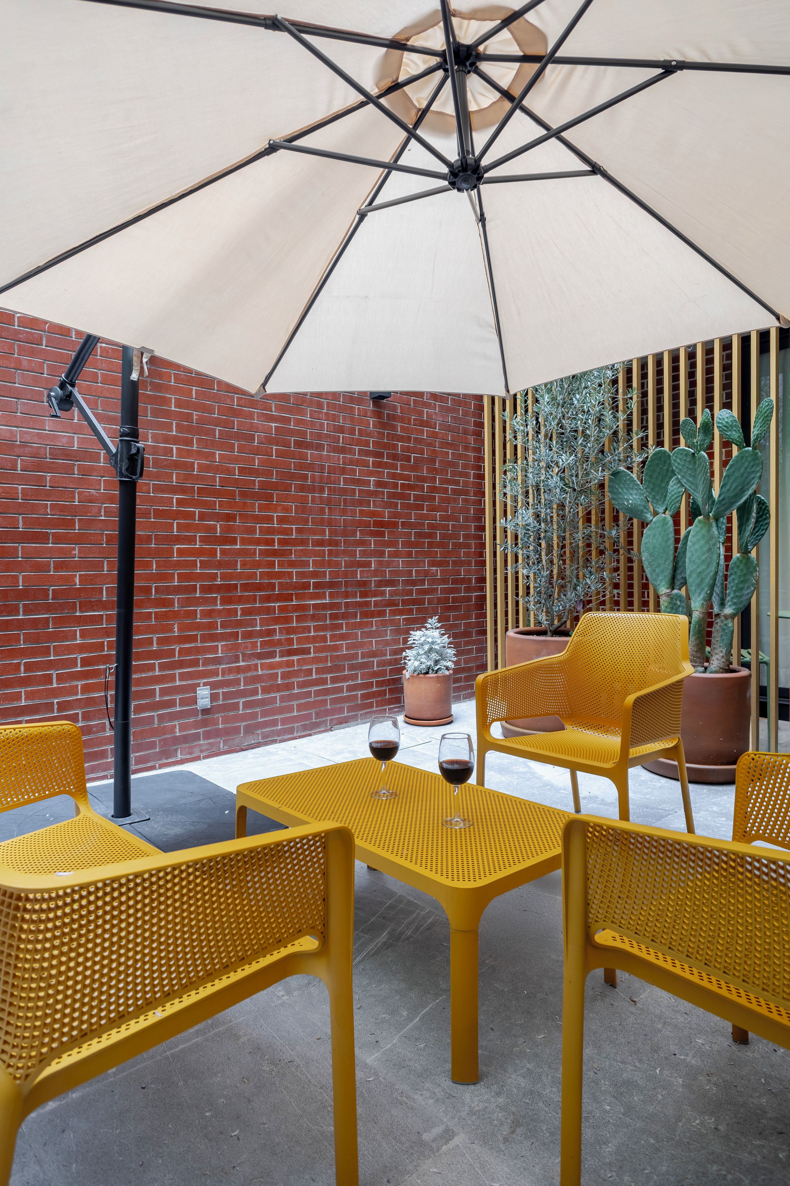 Et udendørs siddeområde med gule stole og et bord, en stor parasol og en kaktus.