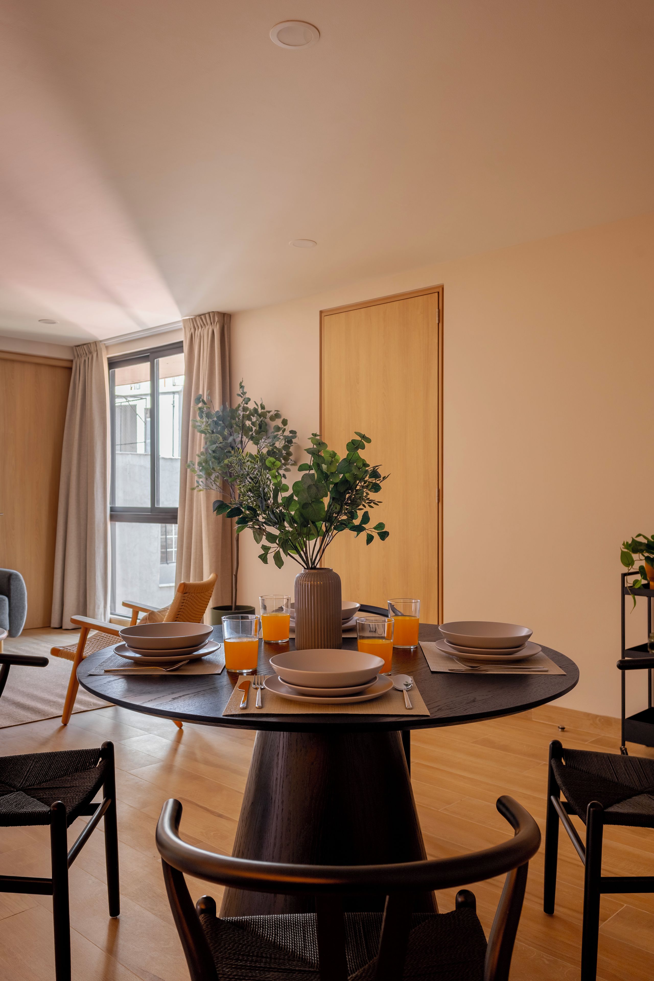 A dining area with a round table, chairs, a vase with plants, and two glasses of orange juice.