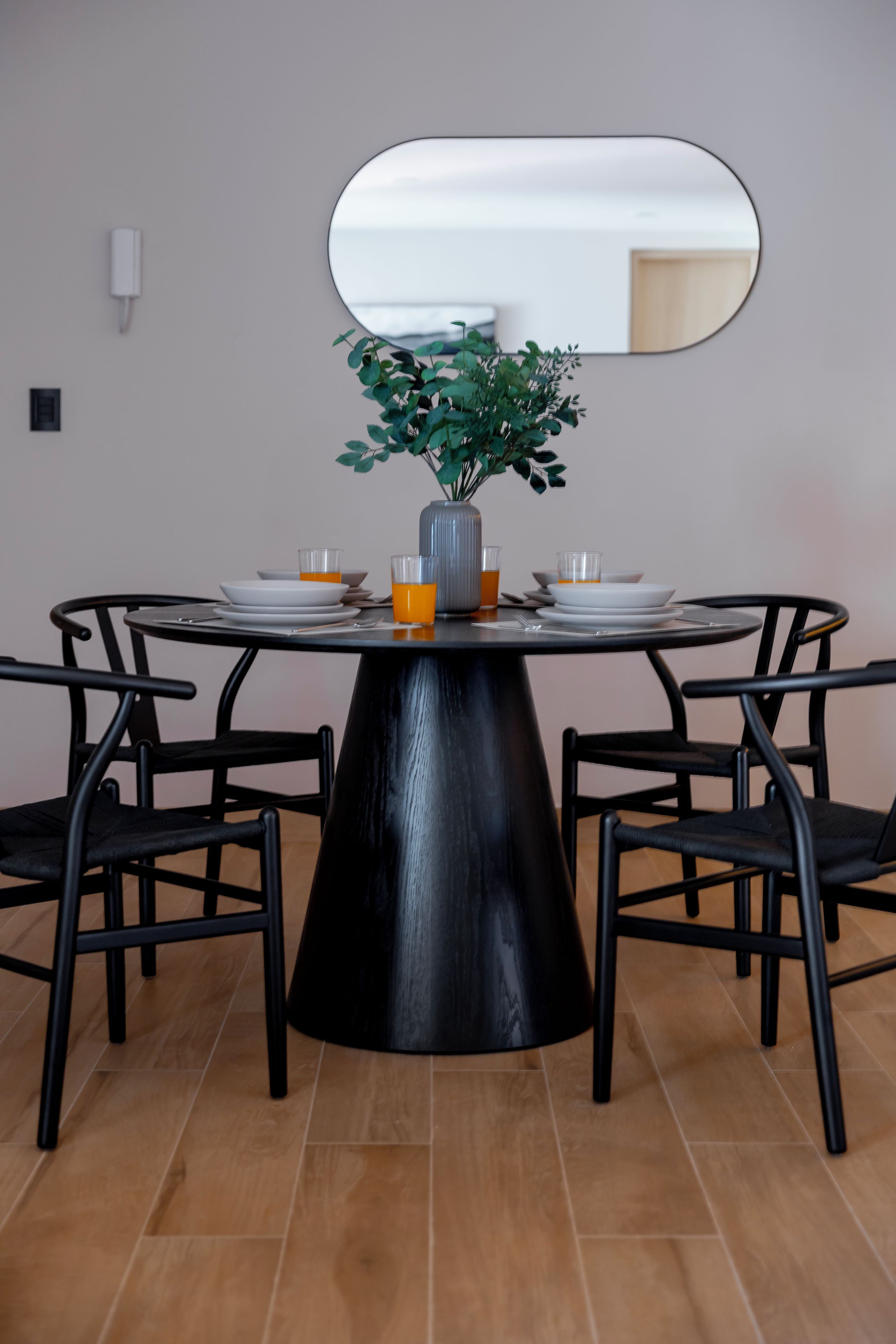 A dining table with four chairs, a vase with green plants, and two glasses of orange juice.