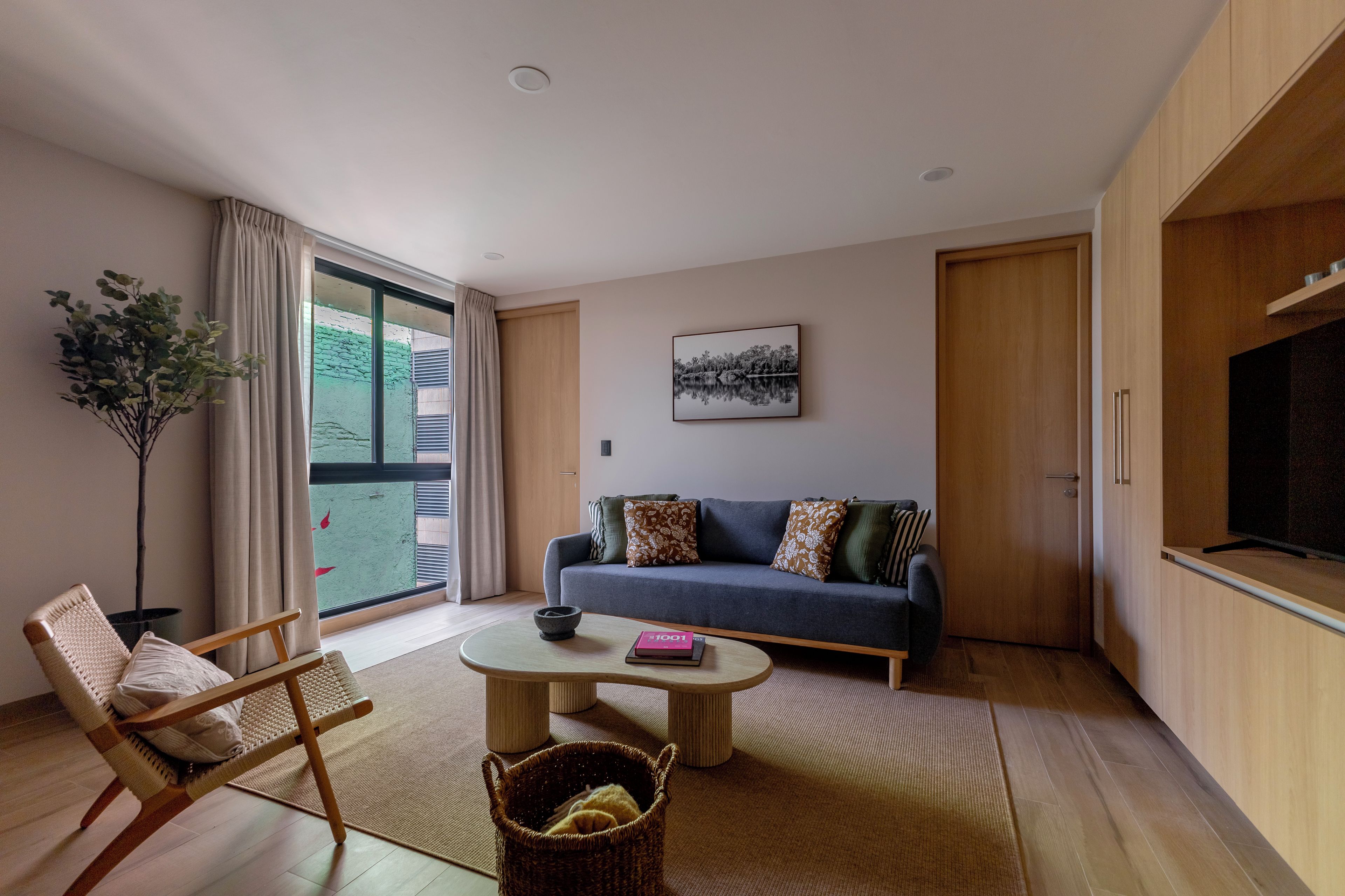 A modern living room with a sofa, a coffee table, a chair, a television, and a large window.