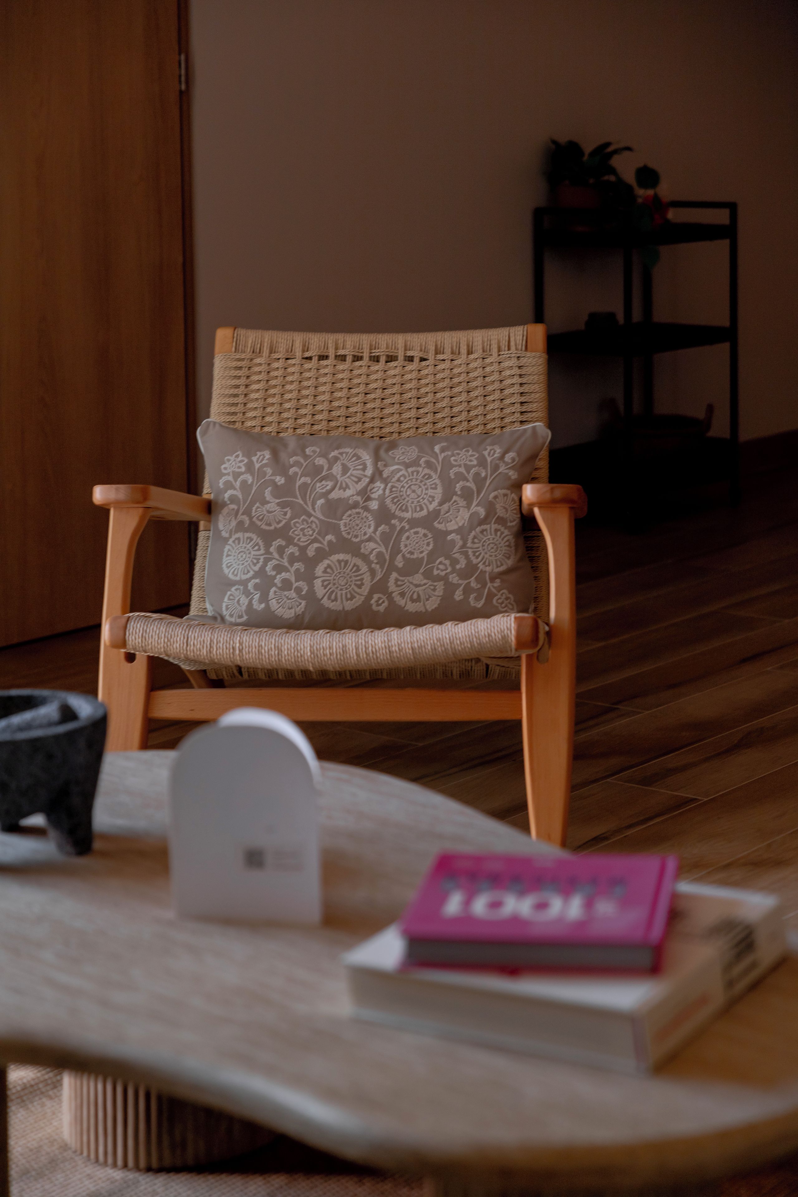 A chair with a woven backrest and a cushion with a floral pattern, placed in a room with wooden flooring.