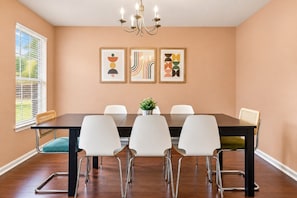 Uma sala de jantar com mesa de madeira escura, cadeiras brancas, um lustre e arte abstrata nas paredes.