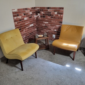 Two yellow armchairs and a small wooden table with a plate and glass in a corner with a brick wall. - Just 0.6 mile to Center of Ojai, this beautiful 3-2 home is calling you. (Ojai)