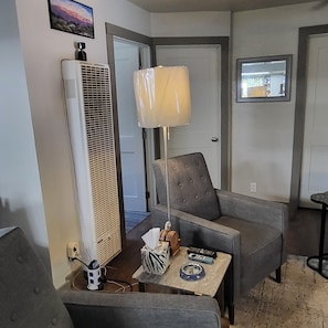 A living room with a grey armchair, a small table with a lamp, and a large air conditioning unit. - Just 0.6 mile to Center of Ojai, this beautiful 3-2 home is calling you. (Ojai)