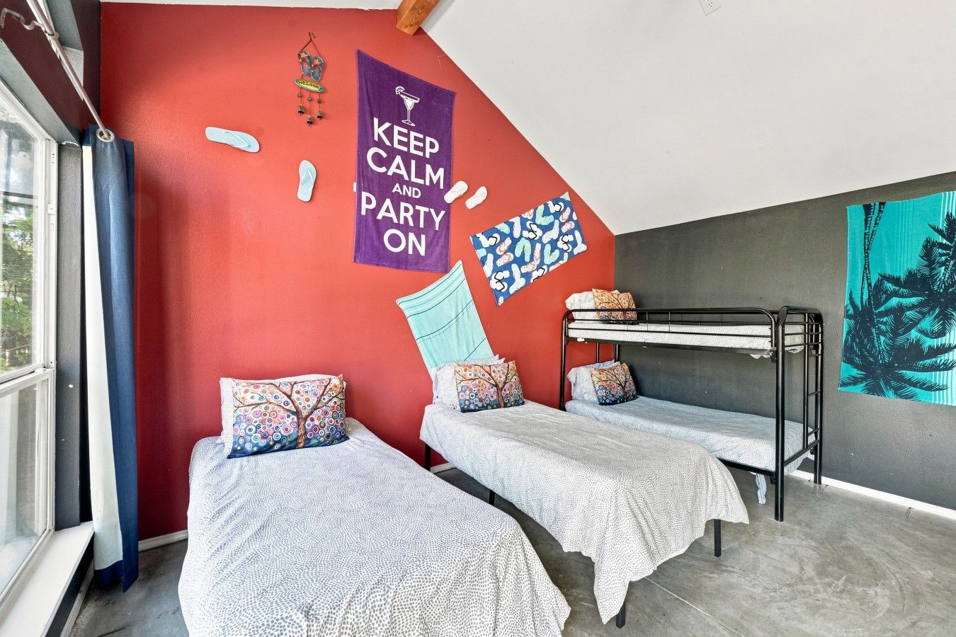 Een kamer met twee stapelbedden, een rode muur, een banner met de tekst 'Keep Calm and Party On' en een muurschildering van tropische bladeren.