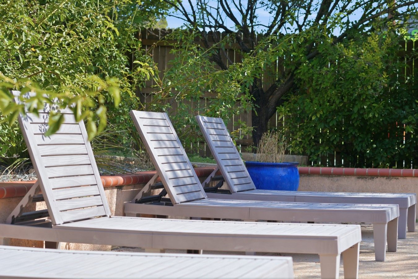 Buitenloungestoelen op een betonnen vloer, omgeven door groen en een houten hek.