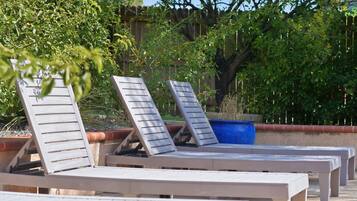 Buitenloungestoelen op een betonnen vloer, omgeven door groen en een houten hek.