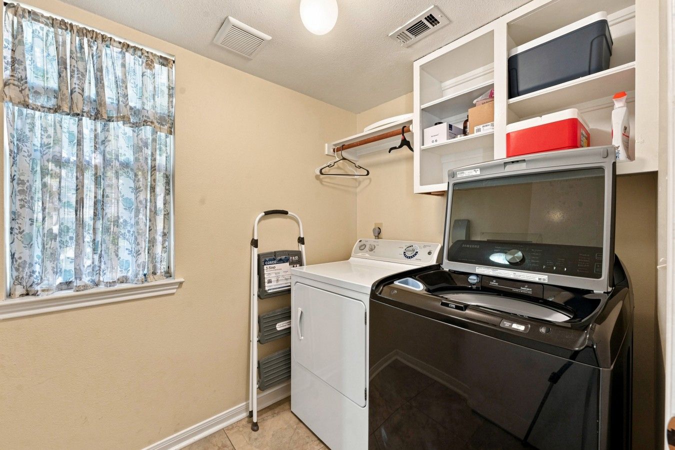 A laundry room with a washing machine, dryer, and a utility cart.