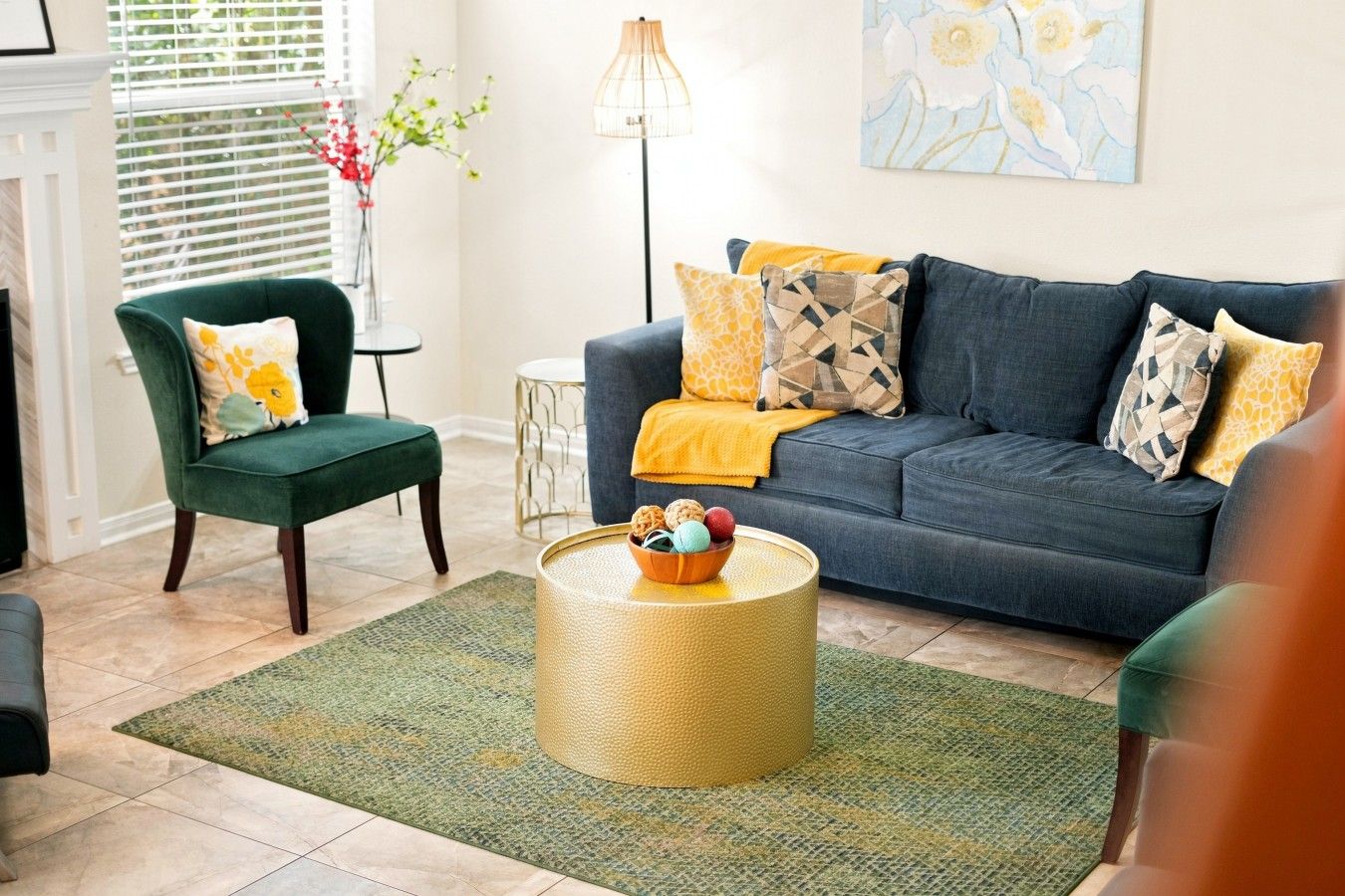 Een zithoek met een donkerblauwe bank, een groene fauteuil en een ronde salontafel met decoratieve objecten.
