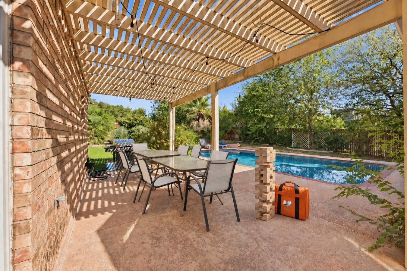 Un patio exterior con piscina, una parrilla y una mesa con sillas.