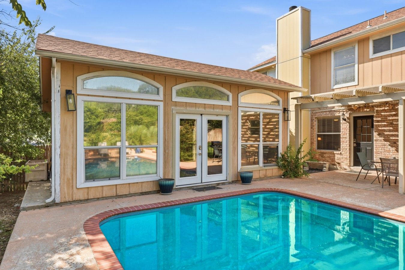 A residential property with a swimming pool, large windows, and a patio area.