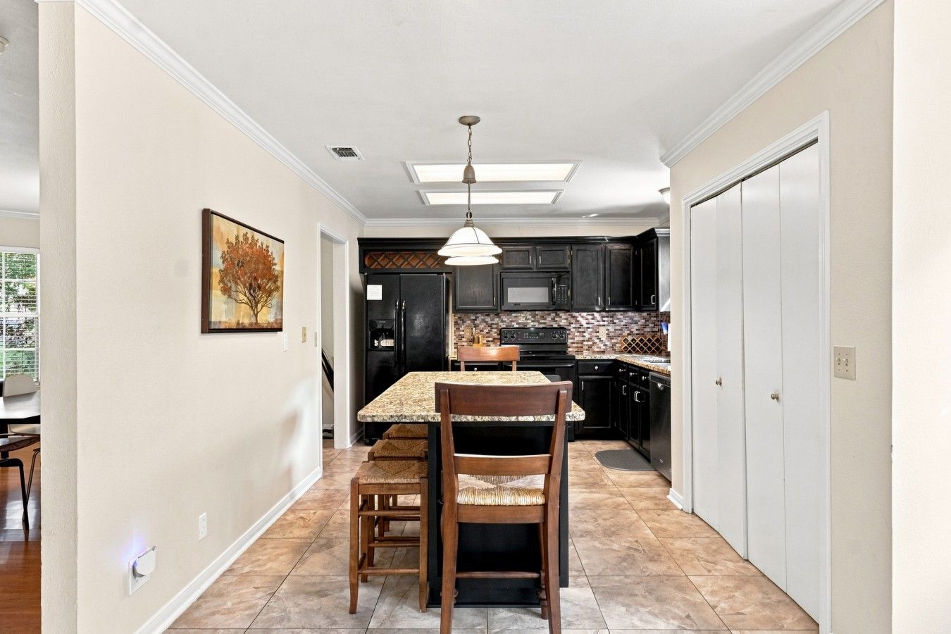 A kitchen with a dining area, featuring a granite countertop, wooden chairs, and a pendant light.