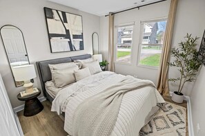 Ein Schlafzimmer mit Bett, Nachttischen, einem Spiegel, einem Fenster mit Aussicht und einer Topfpflanze.