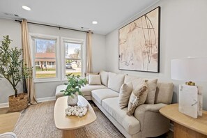 Ein Wohnzimmer mit einer Couch, einem Couchtisch mit Dekoration, einer Topfpflanze und einem großen abstrakten Gemälde an der Wand.