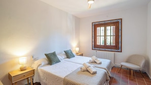 A hotel room with two beds, a chair, a window with a decorative frame, and a bedside table with a lamp. - Heredad La Encarnación Ronda by Ruralidays (Málaga)