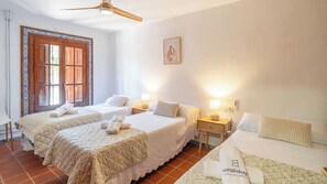 Habitación de hotel con dos camas, una puerta de madera, un ventilador de techo y una lámpara fijada a la pared.