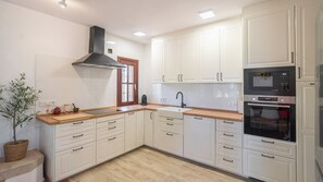 A kitchen with white cabinets, a wooden countertop, a black range hood, a built-in oven, and a sink. - Heredad La Encarnación Ronda by Ruralidays (Málaga)
