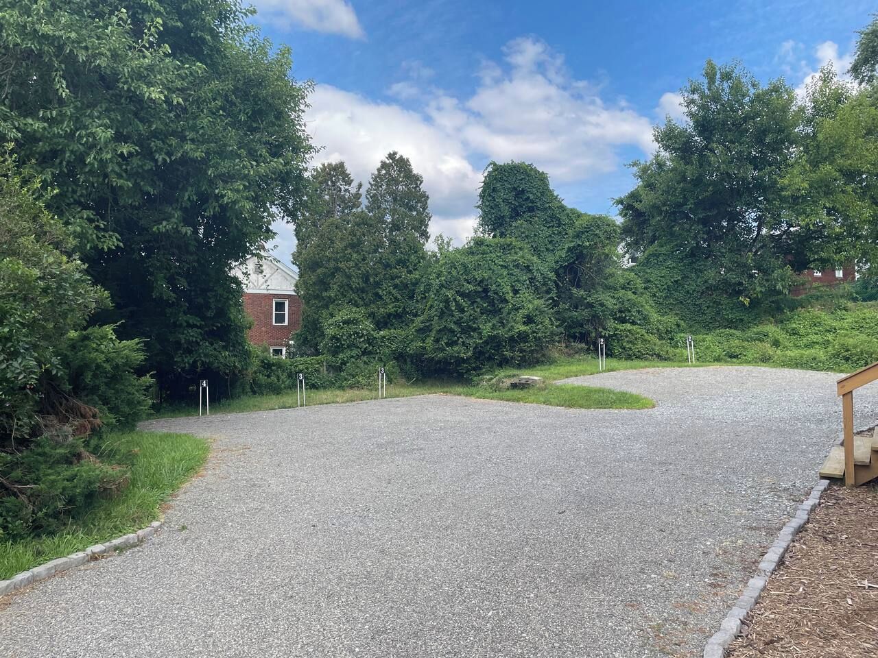 A gravel driveway leading to a building with a red brick facade, surrounded by lush greenery.