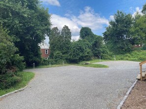 Een grindpad dat leidt naar een gebouw met een rode baksteenvoorgevel, omgeven door weelderige begroeiing.