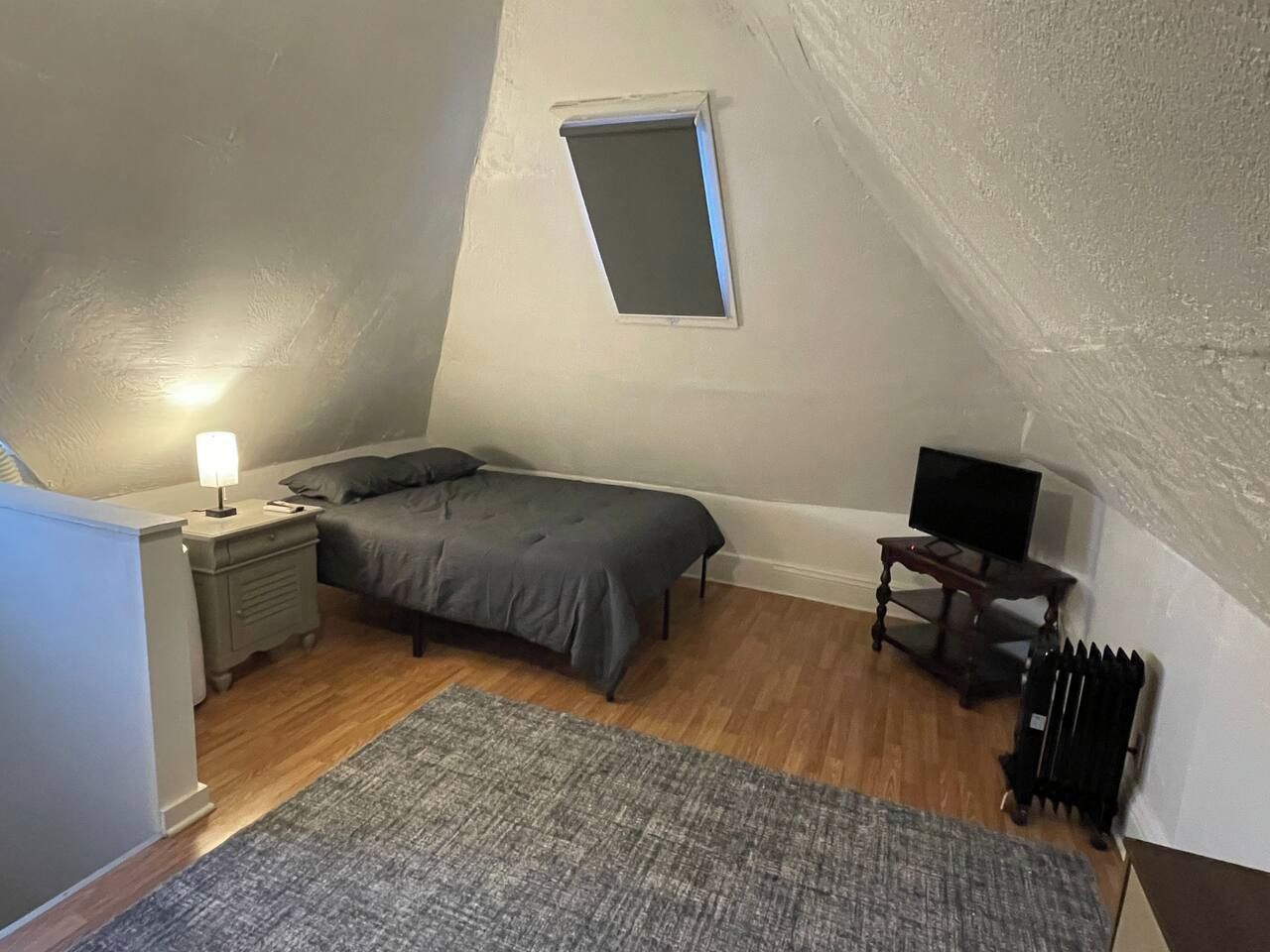 A bedroom with a bed, a nightstand, a lamp, a television, and a radiator.