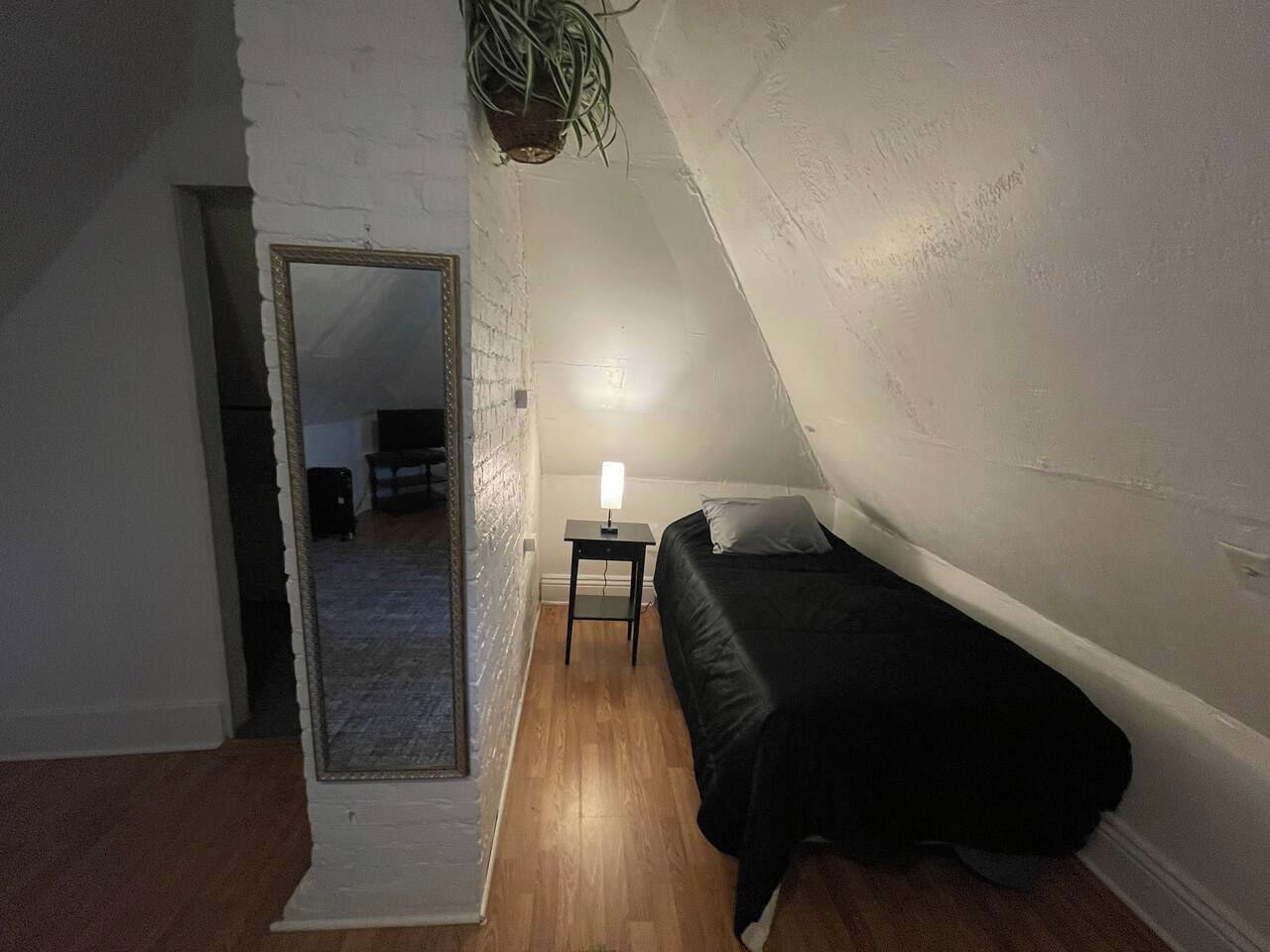 A bedroom with a single bed, a bedside table with a lamp, and a mirror on the wall.