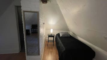 A bedroom with a single bed, a bedside table with a lamp, and a mirror on the wall.