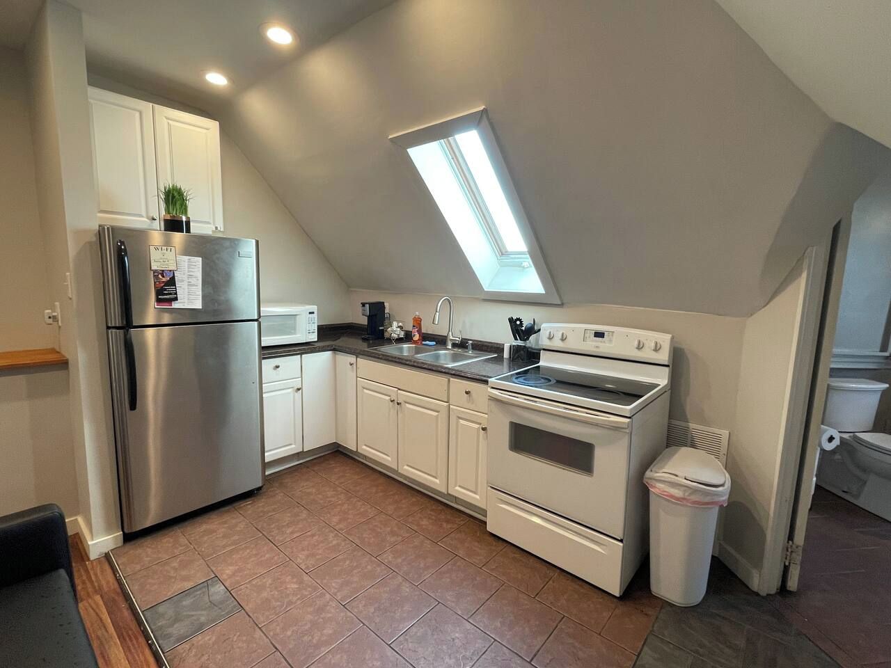 A compact kitchen with a built-in oven, a refrigerator, and a skylight.