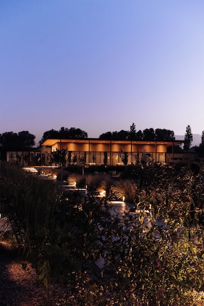 A modern building with a flat roof and large windows, surrounded by a landscaped garden with pathways and plants. - Legado Wine Lodge (Maipú)
