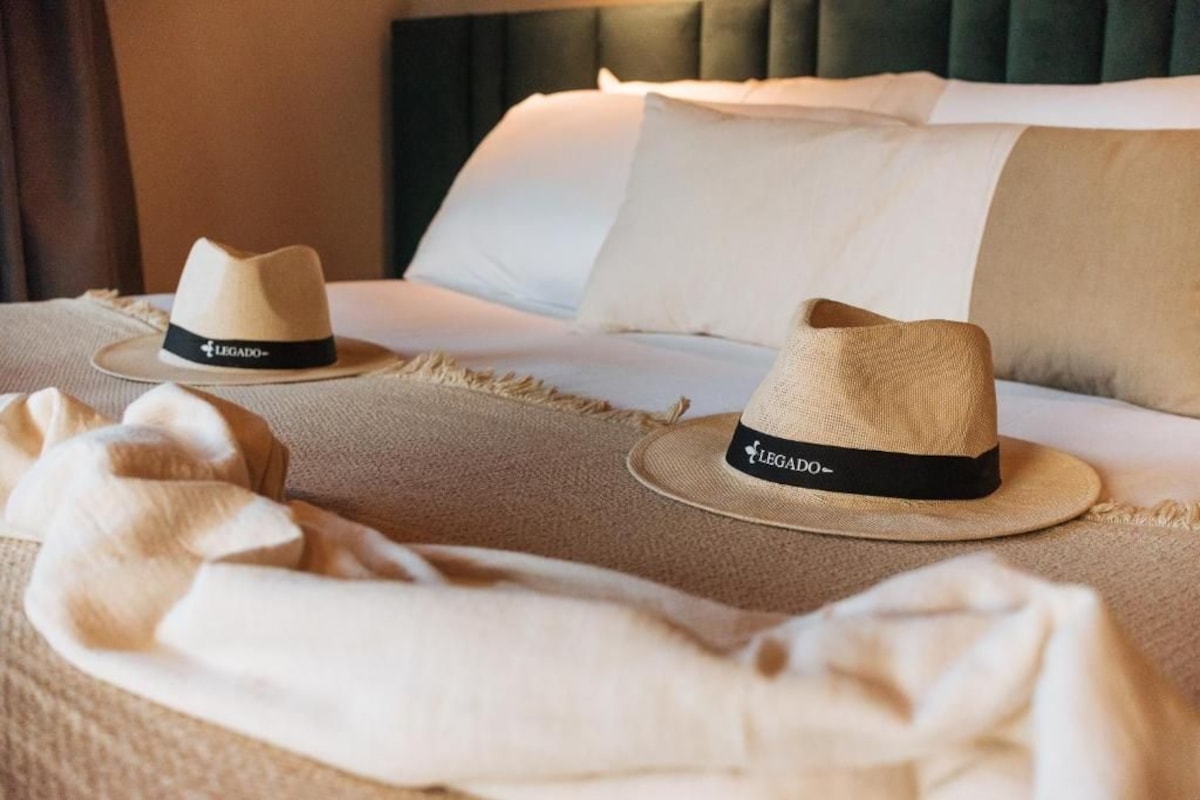 A bed with two hats placed on it, a blanket, and pillows.